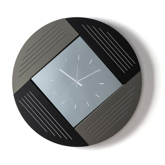 Orologio da parete Oblique dal design geometrico e originale, con struttura circolare in ferro e caratteristico quadrante a rombo in vetro specchiato. Vista frontale, finitura fango/nero/fumé.