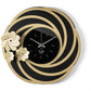 Orologio da parete Tahiti dal design floreale e tridimensionale, con una struttura traforata ispirata a petali stilizzati e tre fiori di diverse dimensioni. Il quadrante in vetro specchiato completa una composizione elegante. Vista frontale. Finitura nero/mile/nero